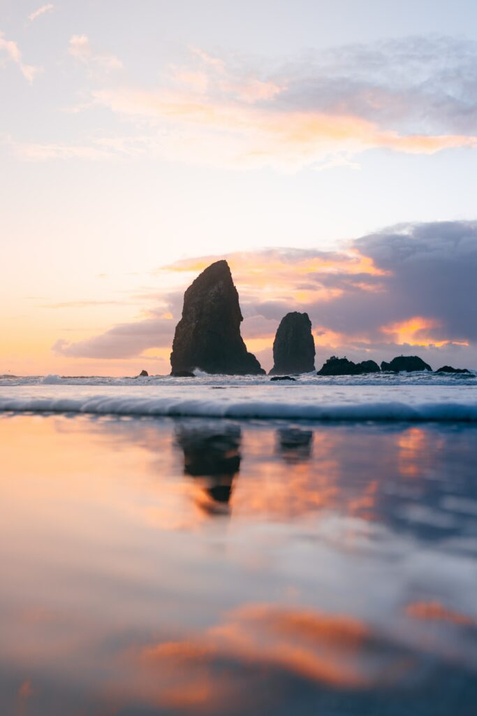 Serene sunset seascape with gentle waves and rugged rocks silhouetted against pastel sky Wallpaper