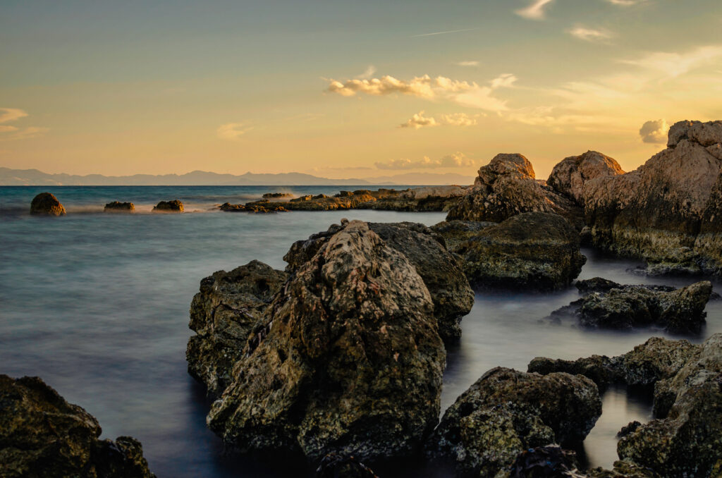 Serene sunset seascape with rocky stones and golden sky reflections on calm misty waters Wallpaper