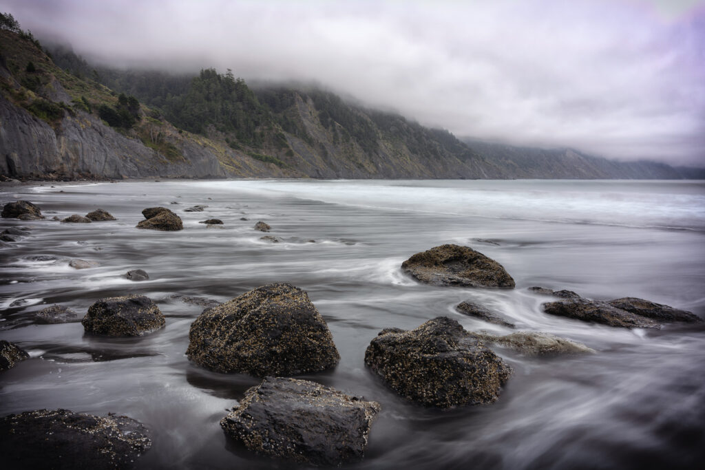 Serene seascape with dark rocks smooth water misty mountains and cloudy sky nature wallpaper background