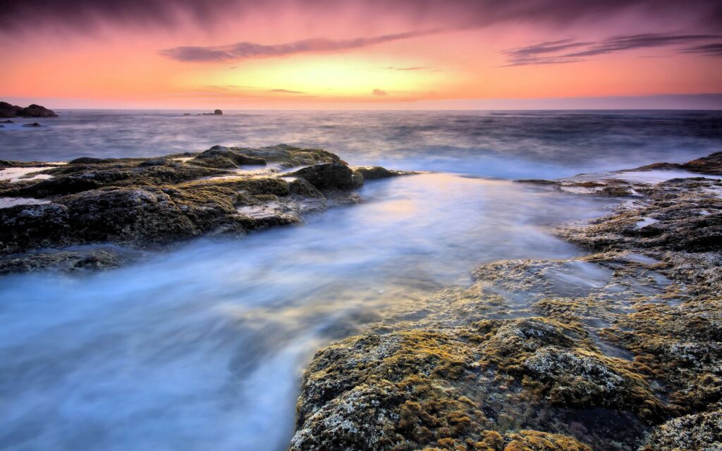 Serene seascape with rugged stones misty fog gentle waves and colorful sunset sky wallpaper