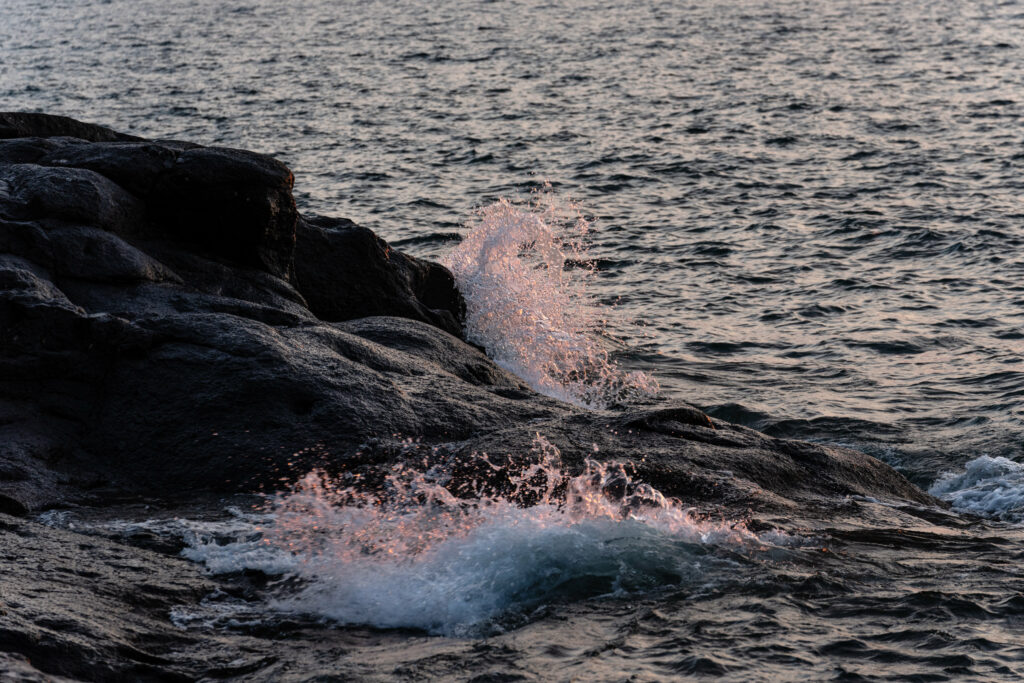 Serene seascape with dark rugged shore stones and gentle seawater splashes in soft light Wallpaper