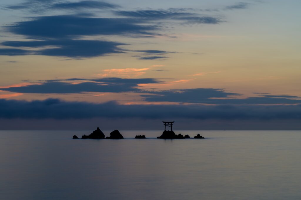 Traditional gate on rocky shore at pastel sunset over calm sea with dramatic clouds wallpaper