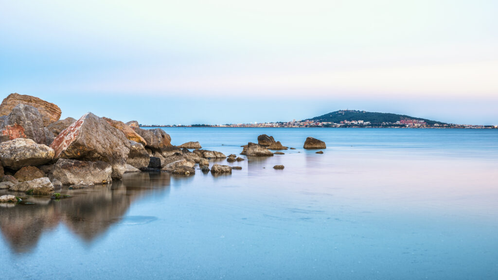 Serene seashore wallpaper with large stones reflecting on calm water in soft pastel tones