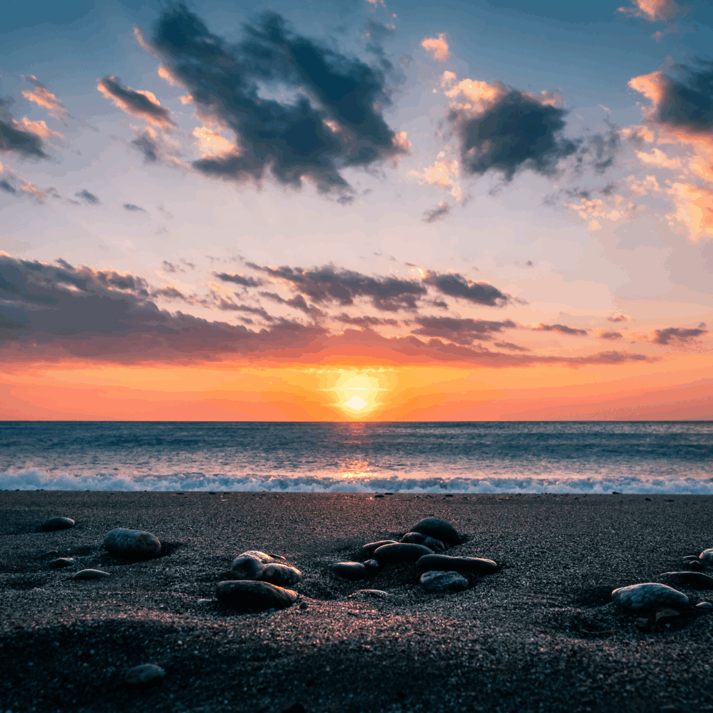 Sunset over calm sea with smooth stones on sandy shore vibrant orange and pink sky wallpaper