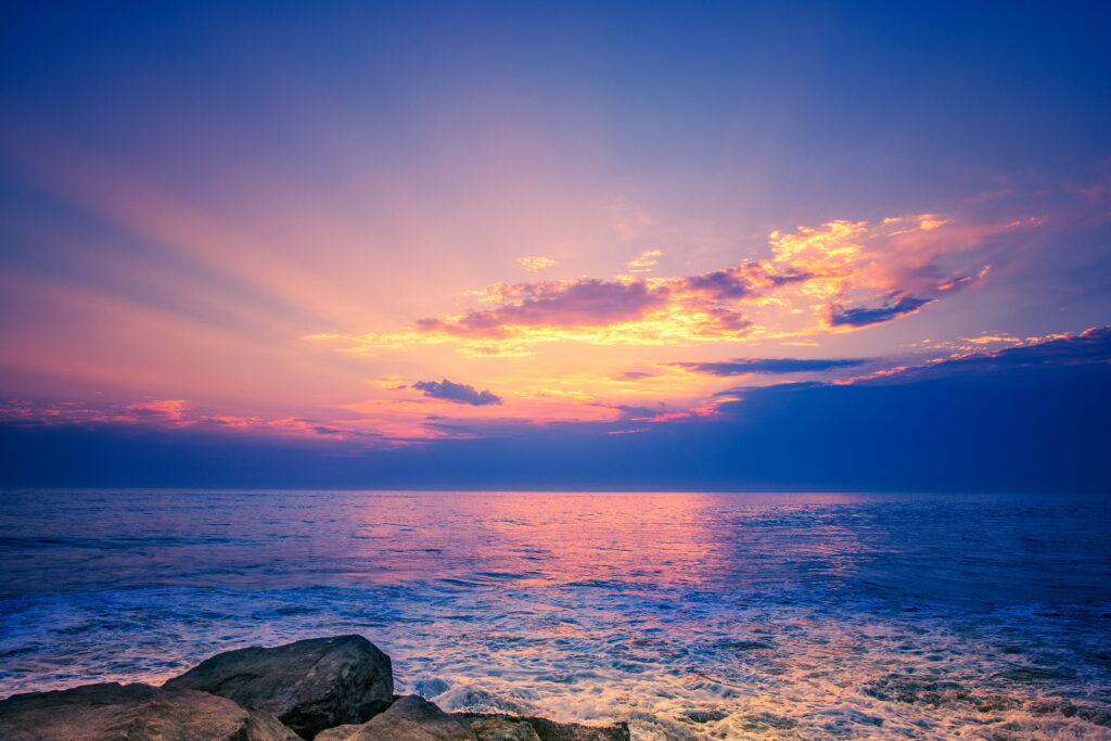 Rugged rocks along peaceful shoreline at sunset with golden pink waves ocean wallpaper background