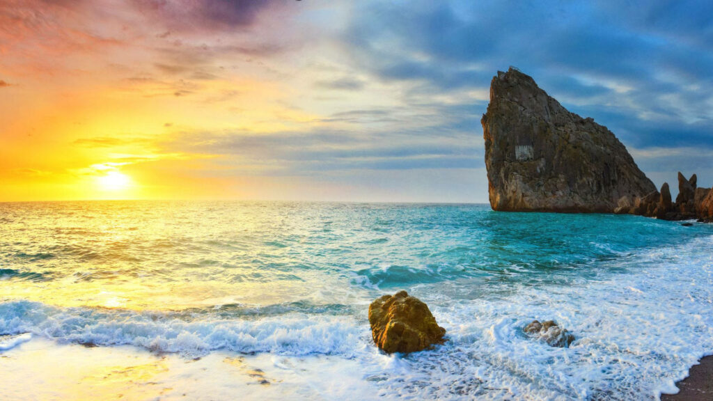 Serene Sunrise: Captivating Beachscape with Majestic Rock Formation and Enchanting Waves Wallpaper