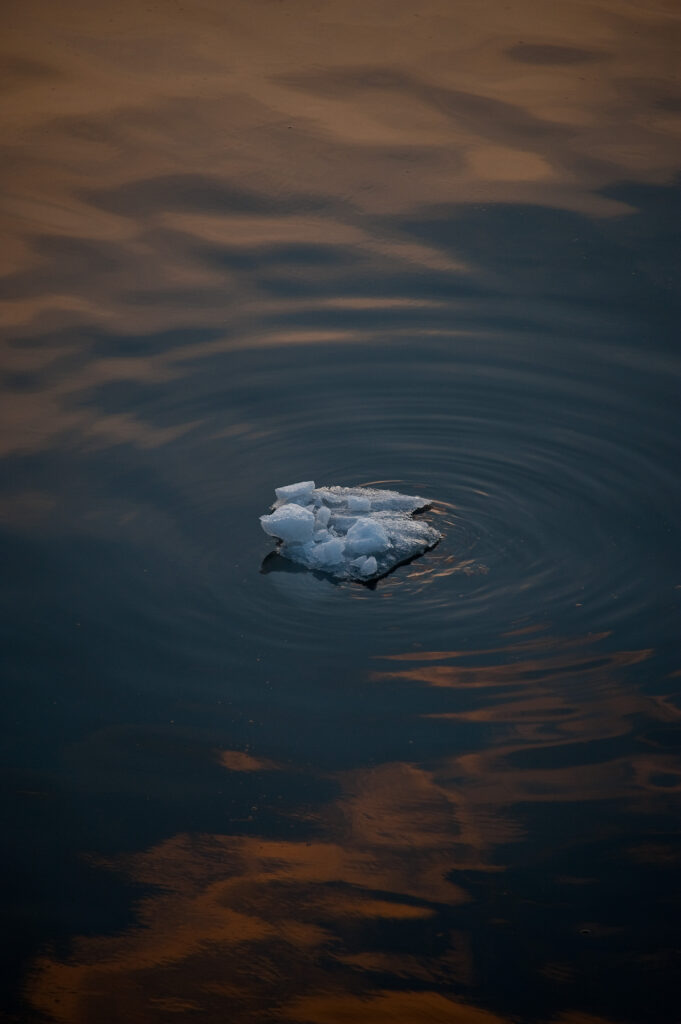 Small iceberg floating on calm water with sunset hues creating gentle circular ripples wallpaper