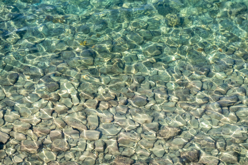 Smooth pebbles under clear water with shimmering light patterns and calming blue green tones wallpaper