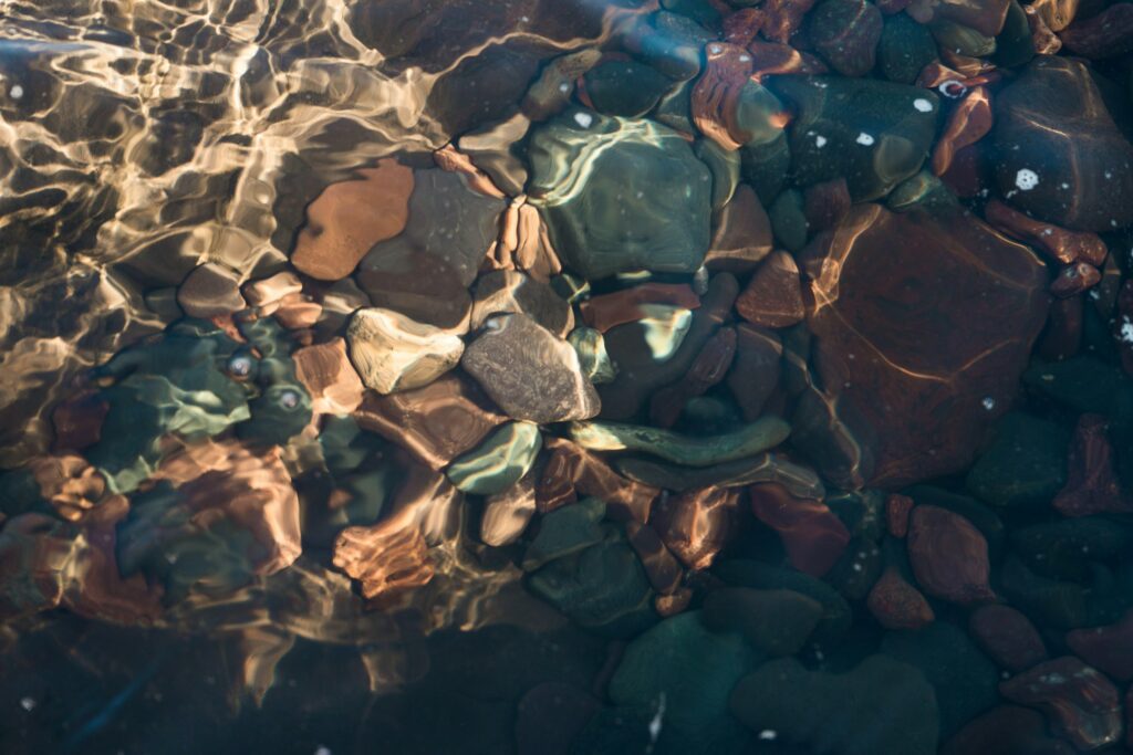 Smooth stones under clear water with sunlight ripples creating a serene natural aquatic scene Wallpaper