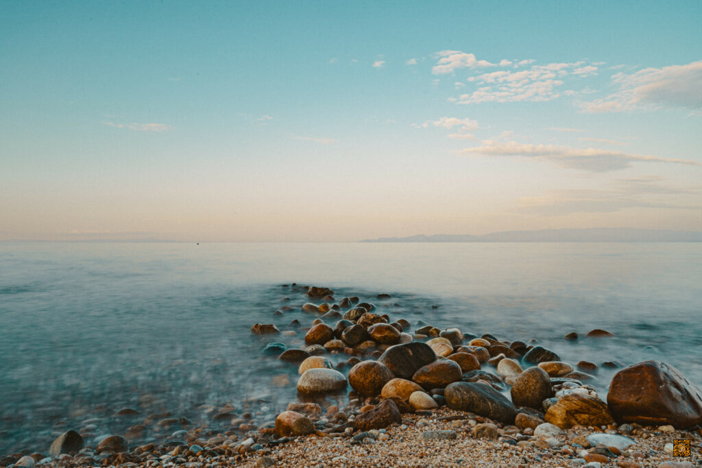 Serene wallpaper with smooth stones pebbles leading into calm sea under pastel sky background