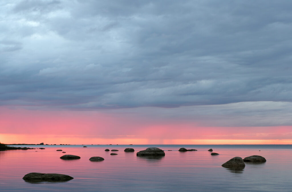 Smooth stones on calm lake reflecting pastel sunset hues with soft clouds serene wallpaper background