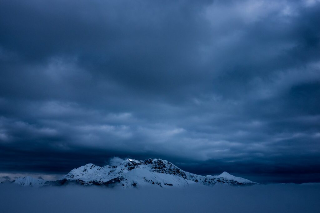 Snow-capped mountain above dense fog under moody sky serene alpine landscape wallpaper background