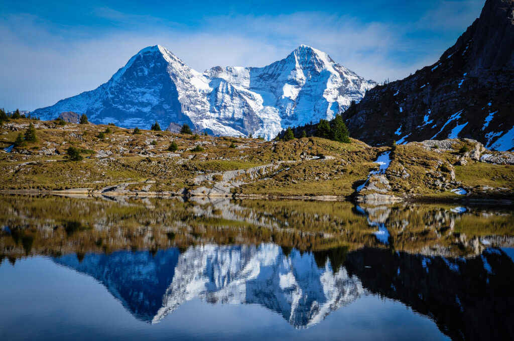 Serene mountain landscape with snow-capped peaks reflected in tranquil lake under blue sky Wallpaper