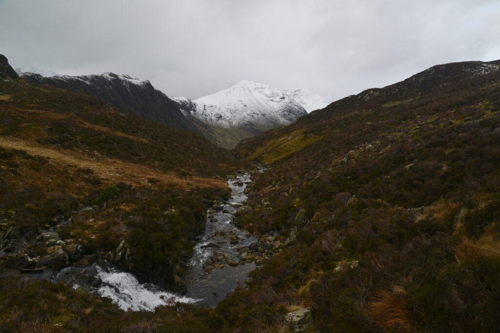 Serene mountain landscape with snow-capped peaks green slopes and clear cascading stream Wallpaper