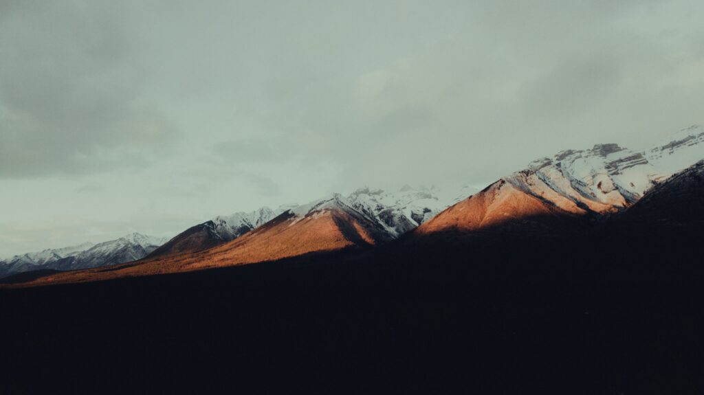 Serene snow-capped mountain range with golden sunlight and dramatic shadows minimalist wallpaper