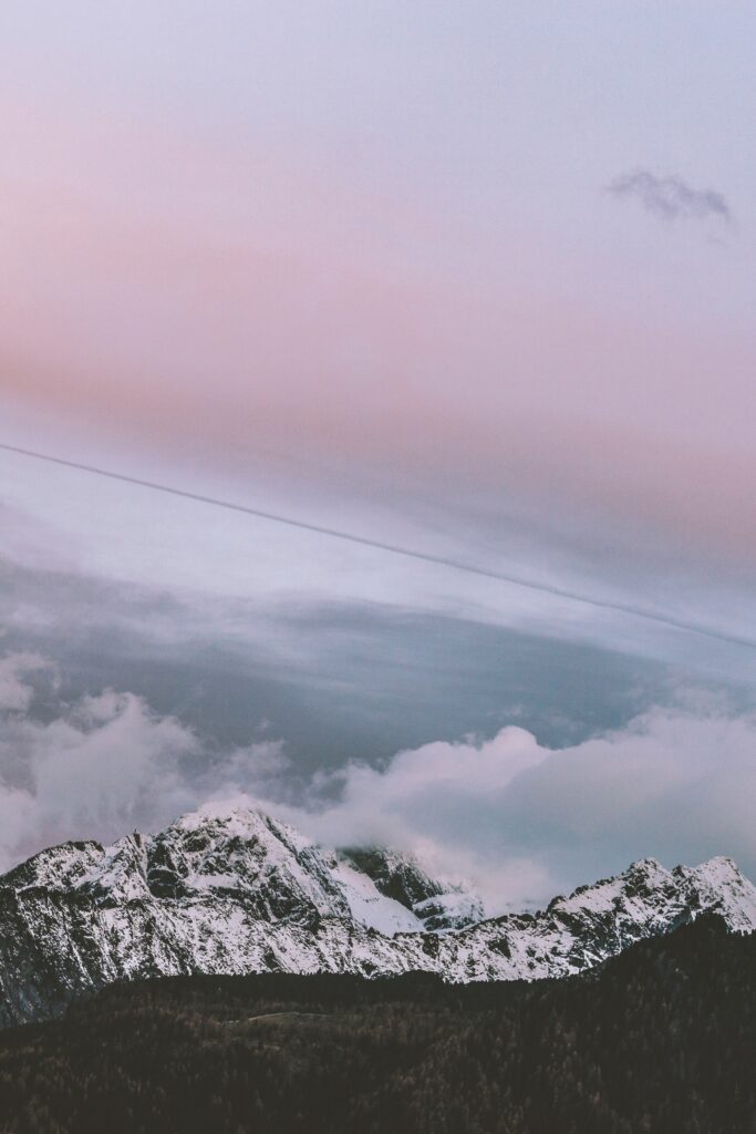 Snow-capped mountains with mist and pastel sunset sky creating a tranquil winter scene wallpaper