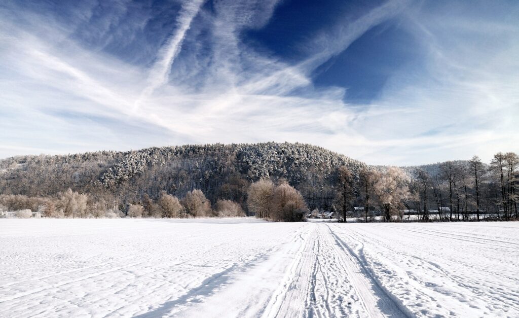 Snowy country road with tire tracks through frosted fields and trees under blue sky background Wallpaper