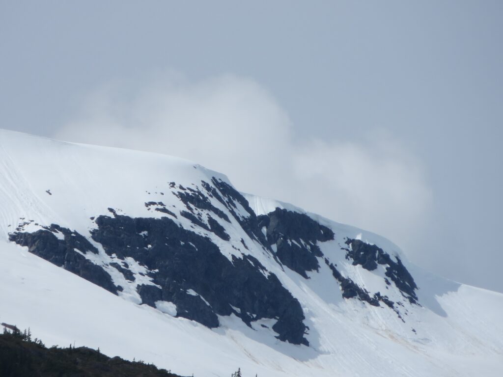 Snow-covered mountain peak with rugged dark rocks under soft sky winter landscape wallpaper