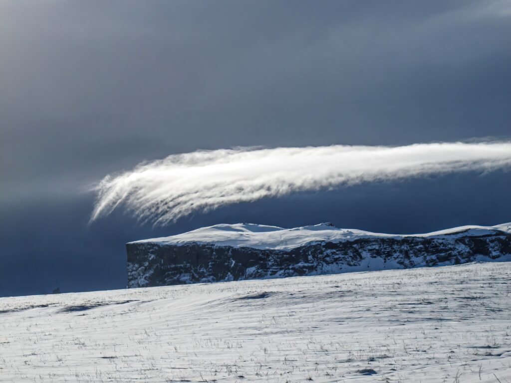 Snow-covered mountain under dramatic sky with sweeping clouds serene winter landscape wallpaper