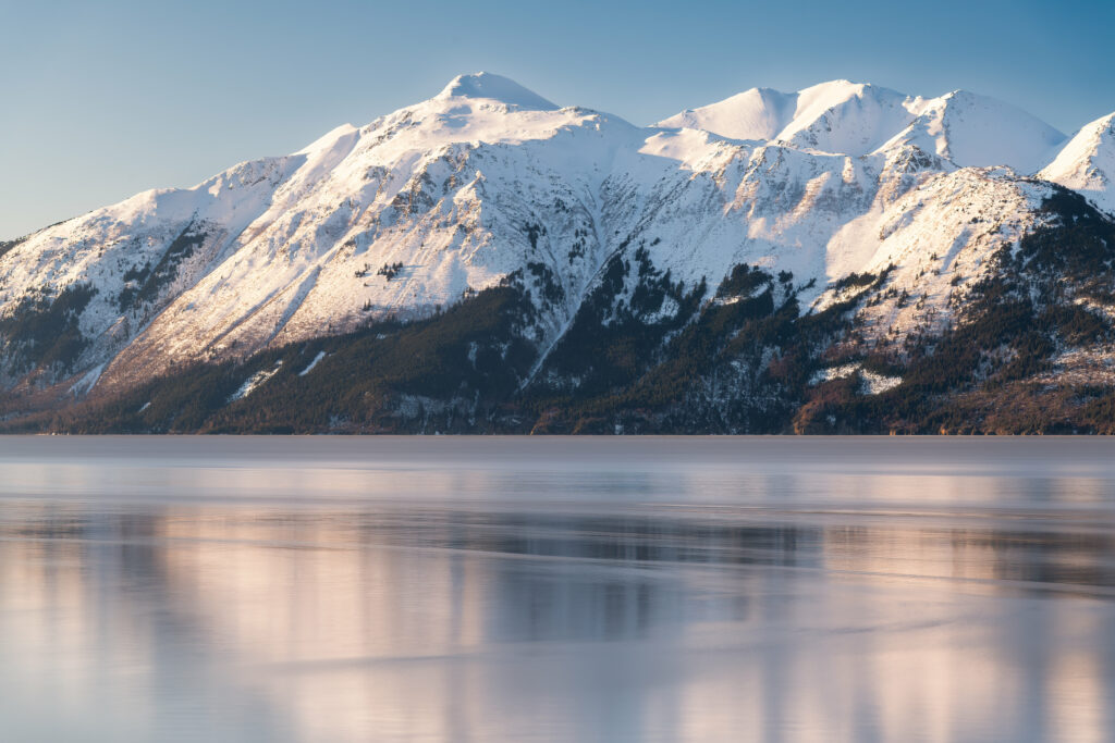 Snow-covered mountains reflected in calm lake under golden sunlight serene winter landscape wallpaper