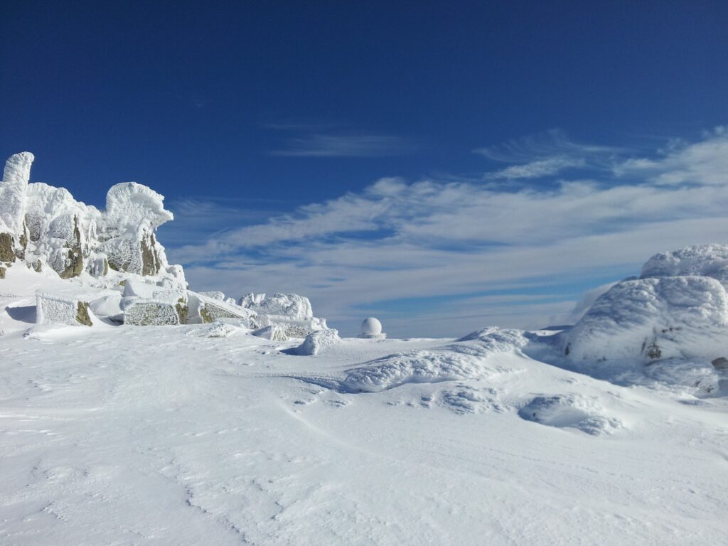 Serene snow-covered mountains under deep blue sky with icy rocks and wispy clouds winter wallpaper