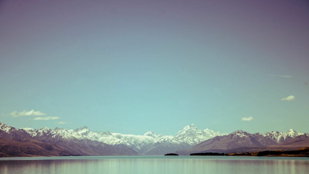 Serene mountain landscape with snow-capped peaks reflecting on a calm lake under blue sky Wallpaper