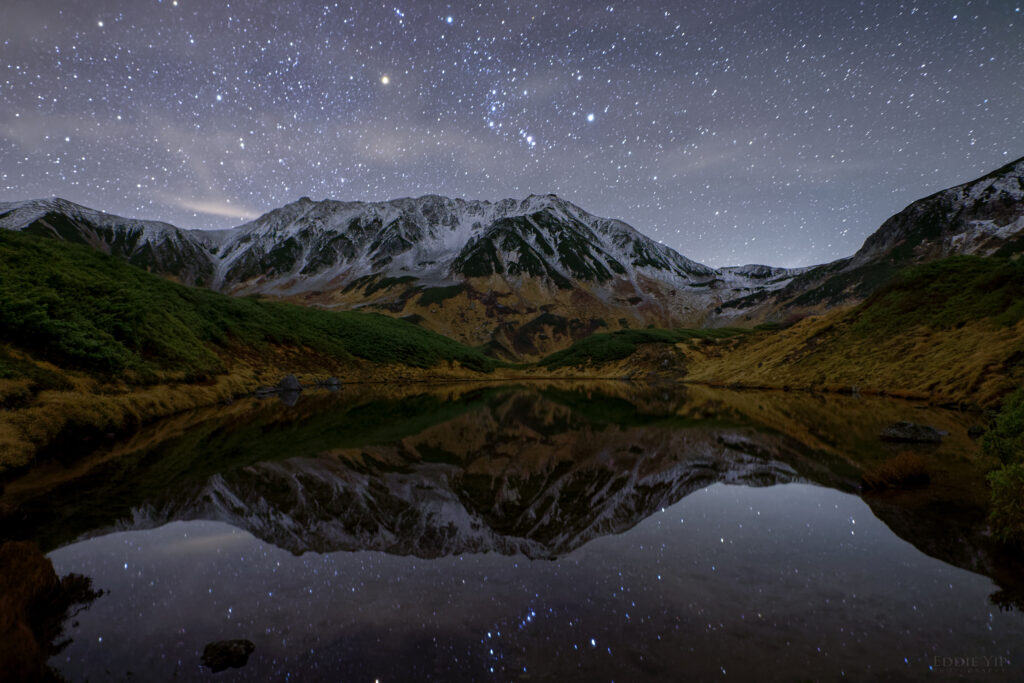 Serene night landscape with snow-capped mountains reflected in a still lake under starry sky Wallpaper