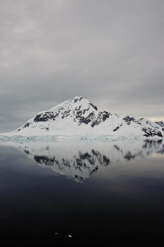 Snow-capped mountain reflected in calm ocean with cloudy sky minimalist peaceful wallpaper