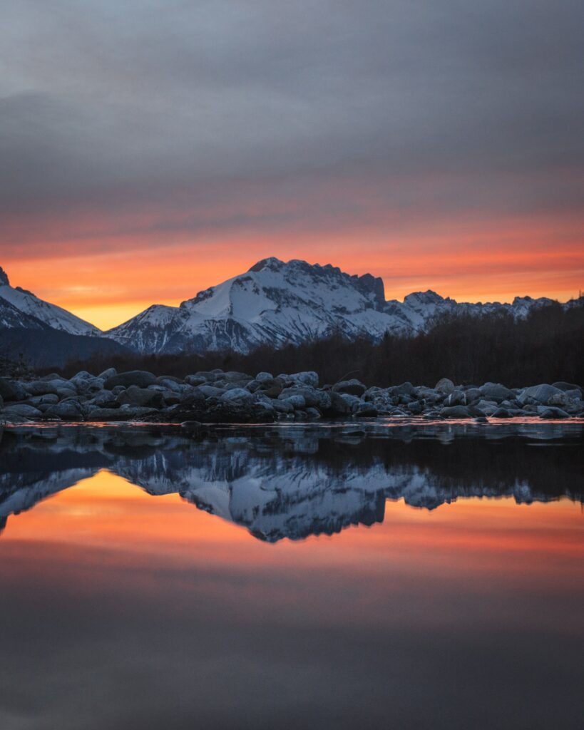 Snow-capped mountains reflected in calm lake at vibrant orange and purple sunset twilight wallpaper