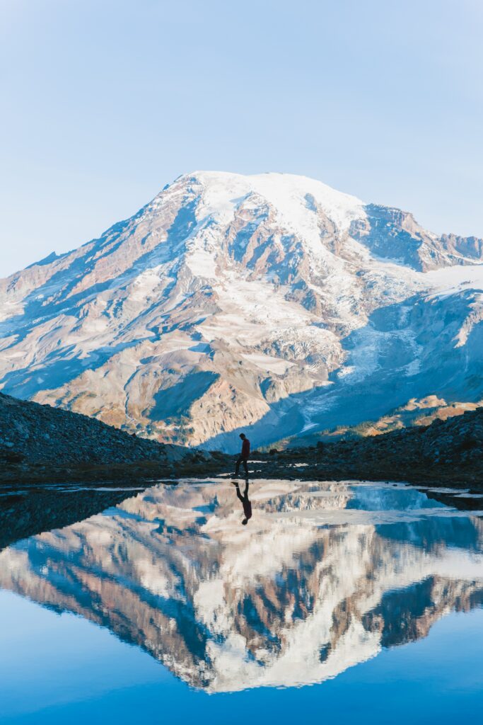 Snow-capped mountain mirrored in lake with solitary figure under clear blue sky landscape wallpaper