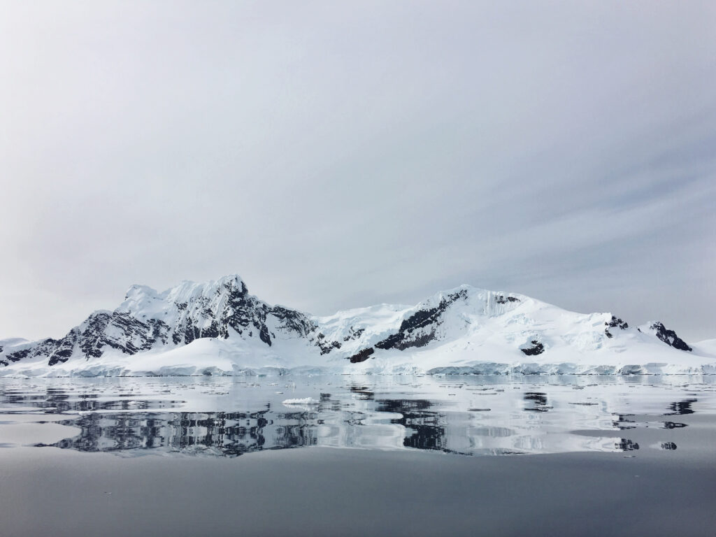 Serene winter wallpaper with snow-capped mountains reflected in calm lake under overcast sky