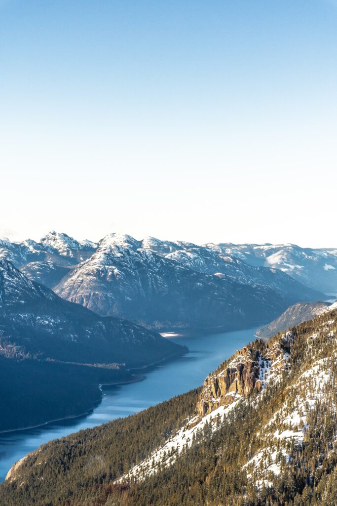 Snow-capped mountains with winding river and forested slopes under clear blue sky wallpaper