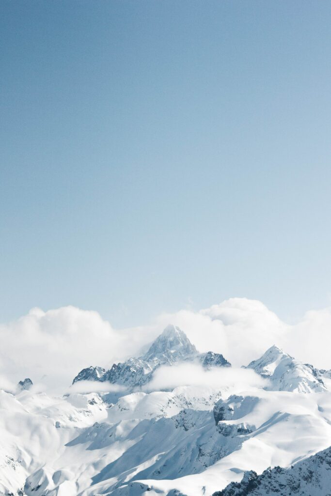 Snow-covered mountain peak with soft clouds under blue sky winter wonderland landscape wallpaper
