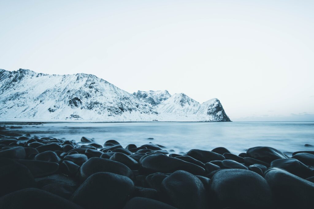 Snowy mountains reflected in calm lake with smooth stones minimal winter landscape wallpaper