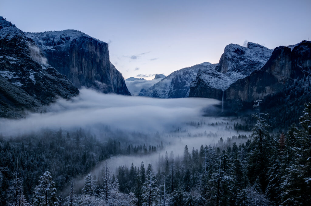 Winter landscape with snow-covered mountains misty forest and rugged rocks in blue tones Wallpaper