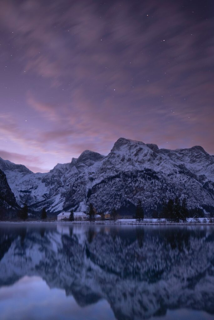 Serene dusk mountain landscape with snow peaks reflected in calm lake under purple blue sky Wallpaper