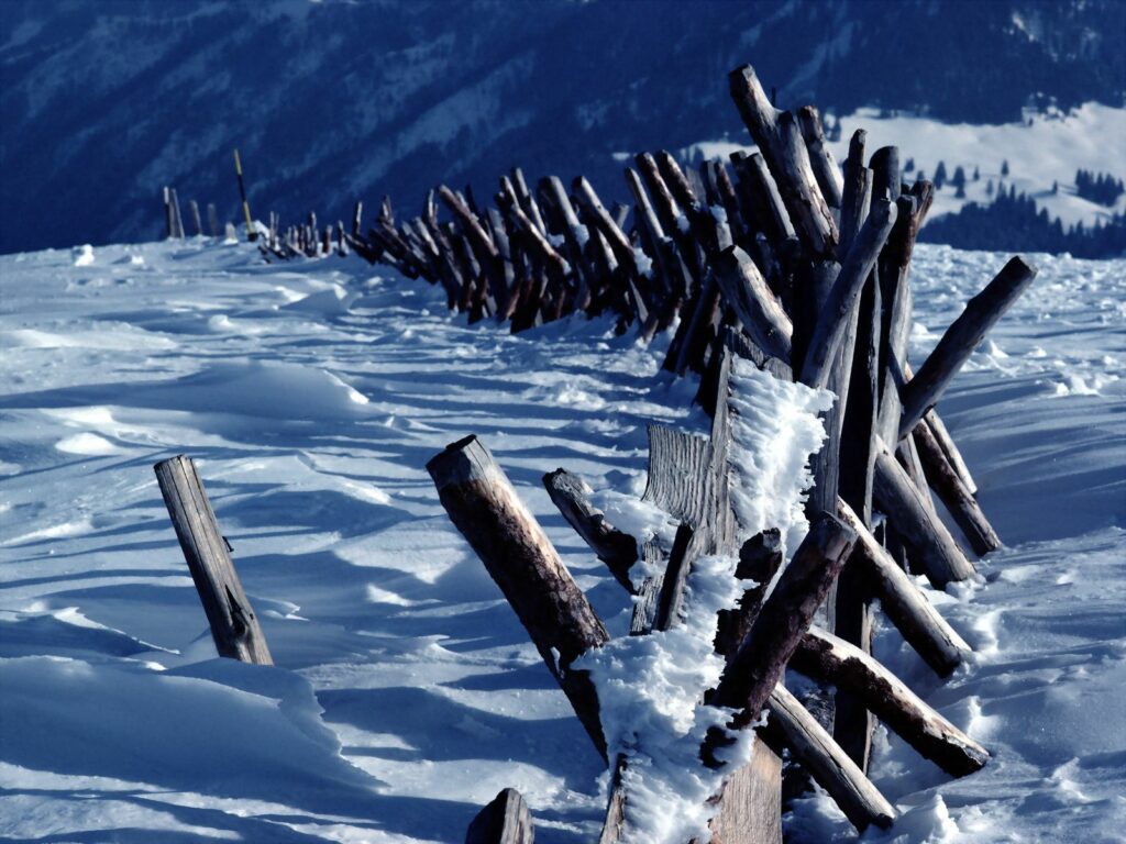 Rustic wooden log fence in snowy mountain landscape with white snow and blue sky background Wallpaper