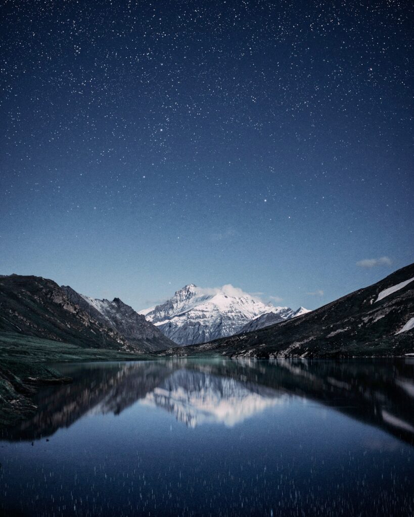 Snowy mountain peaks reflect in a calm lake under a starry night sky serene nature wallpaper