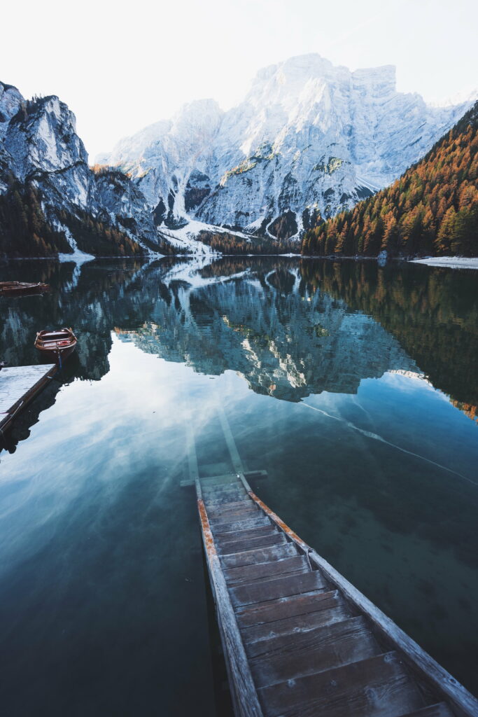 Majestic Winter Wonderland: A Captivating HD Phone Wallpaper of a Snow-covered Boat amidst Serene Mountains and Reflections on Crystal Clear Water