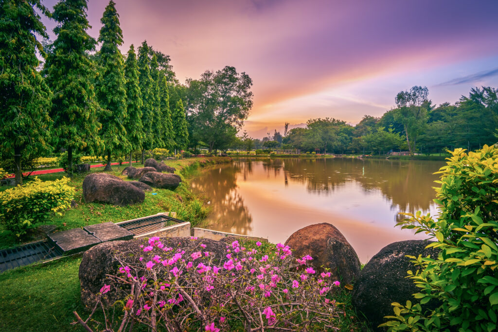 Tranquil spring lake reflecting colorful sunset sky with lush trees pink flowers and rocks Wallpaper