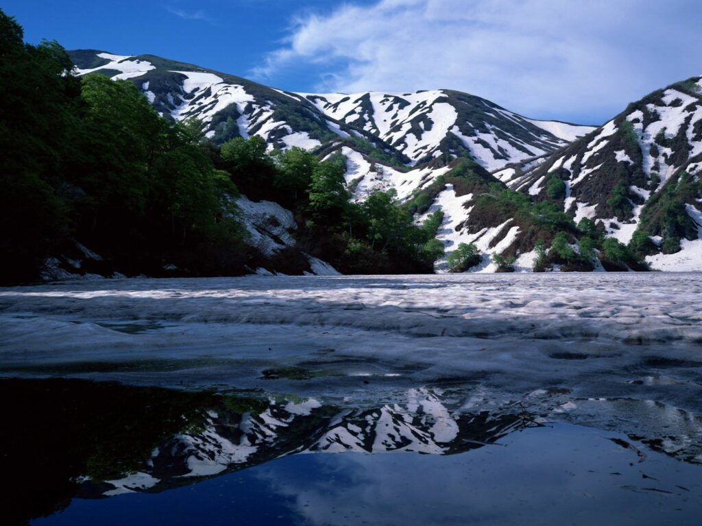 Serene spring mountain landscape with snowcaps lush green trees mirrored in calm lake wallpaper