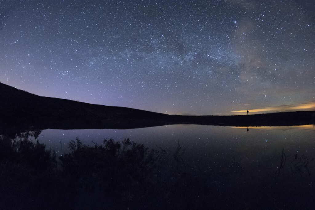 Starry night sky reflected on calm lake with silhouette by shore peaceful nature wallpaper