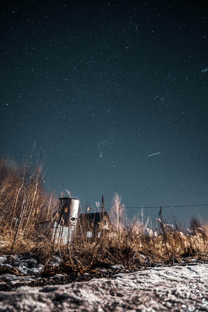 Abandoned countryside at night with starry sky rustic bushes and old buildings in moonlight wallpaper
