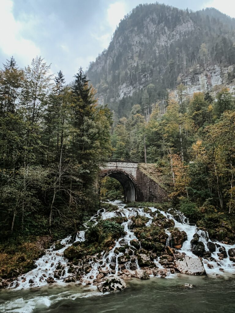 Stone arch bridge over waterfall with lush forest and misty mountain scenic landscape wallpaper
