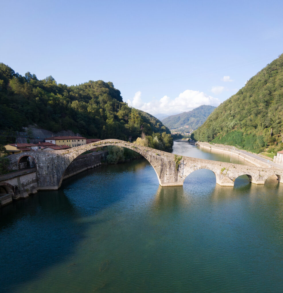 Stone bridge over calm river surrounded by green trees rolling hills and clear blue sky wallpaper