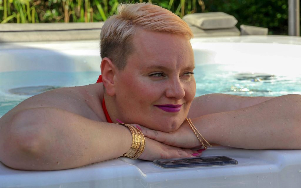 Plus-size woman with blonde hair and purple lipstick relaxing in sunny jacuzzi with red top Wallpaper