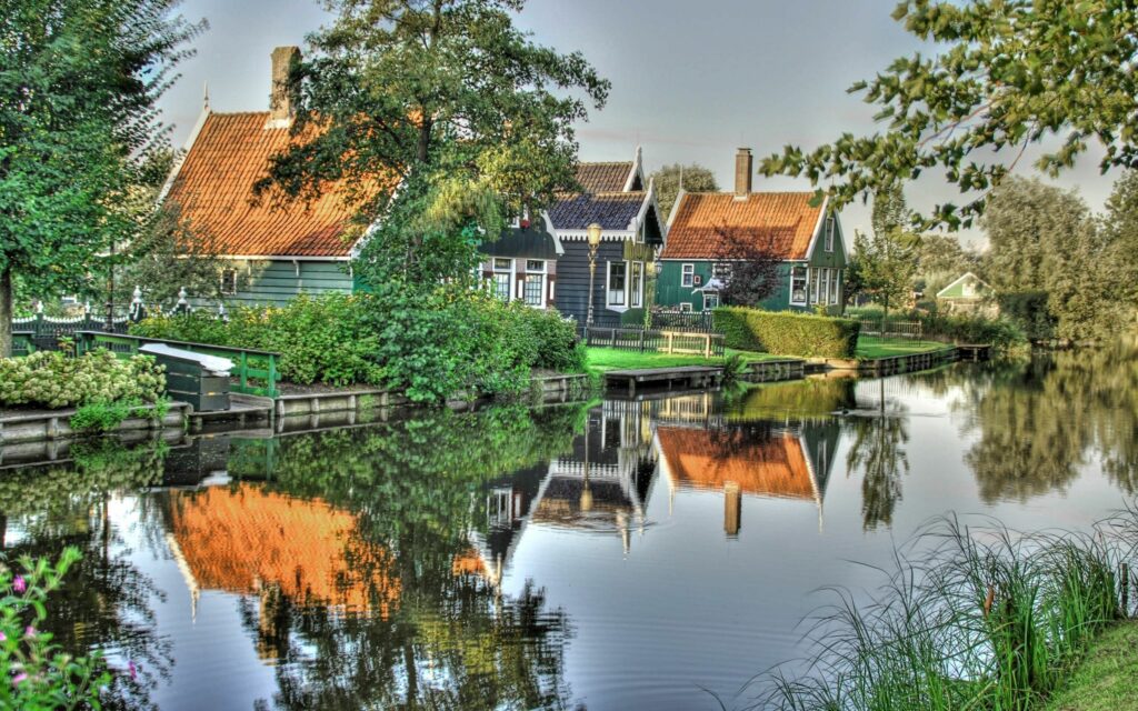 Colorful riverside lodges with lush greenery reflected in calm water serene summer wallpaper