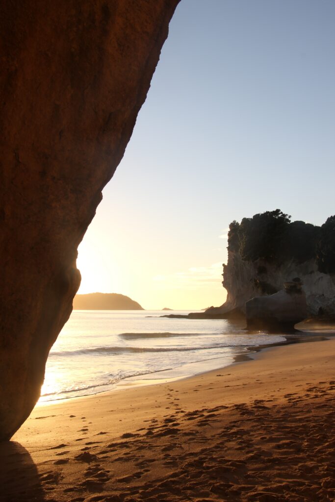 Serene coastal sunrise with rugged rocks soft sand footprints and gentle waves on shore wallpaper