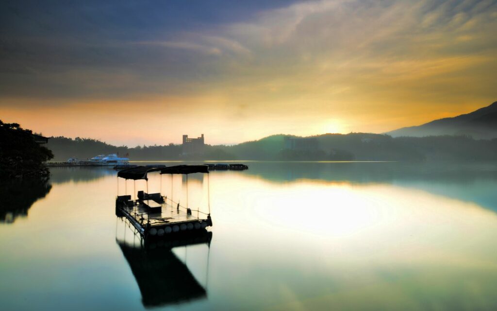 Peaceful raft on calm lake at sunrise with morning fog and gentle mountains in background Wallpaper