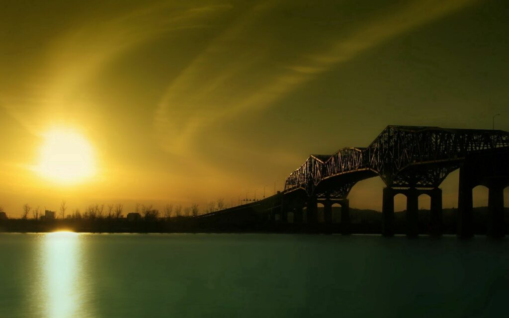 Sunrise over tranquil river with dramatic silhouetted bridge and golden sky wallpaper background